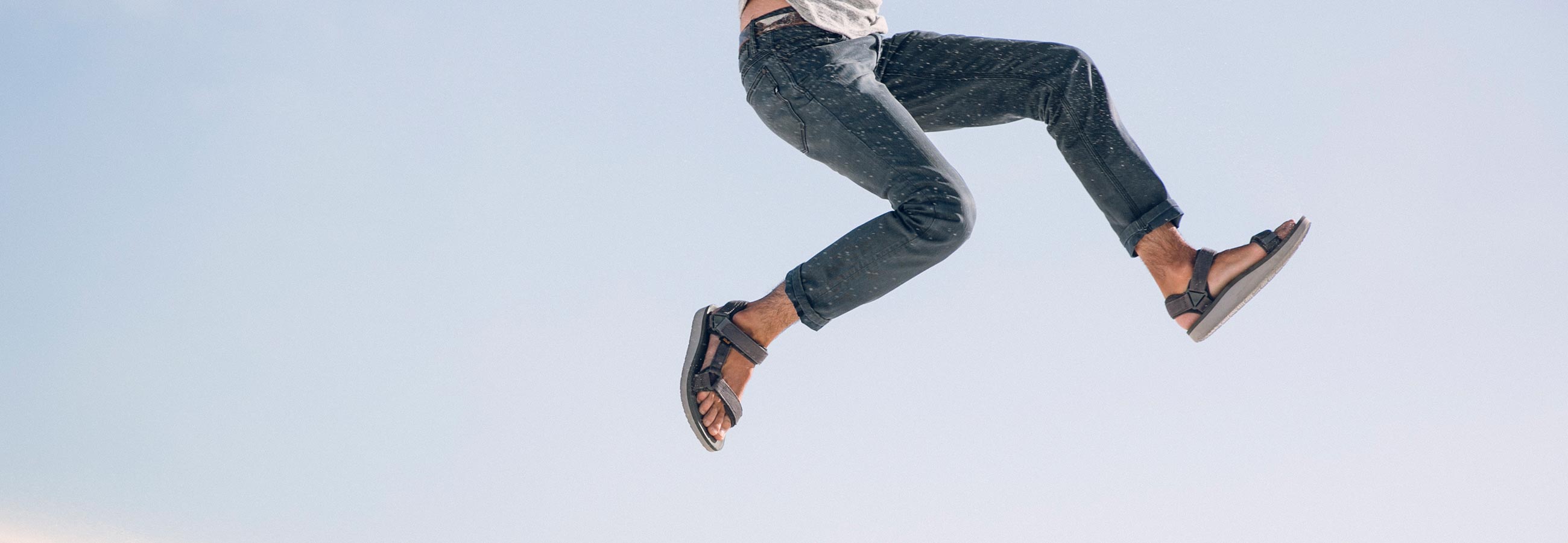 Man wearing jeans and Teva sandals leaping in the air.