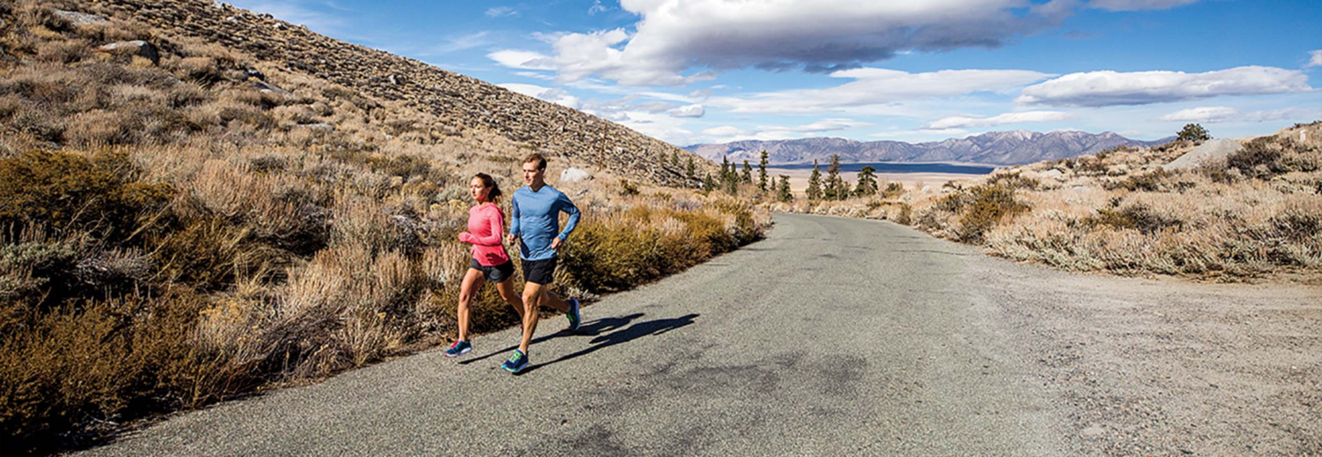 A man and a woman wearing Hoka One One shoes running on a gravel trail.