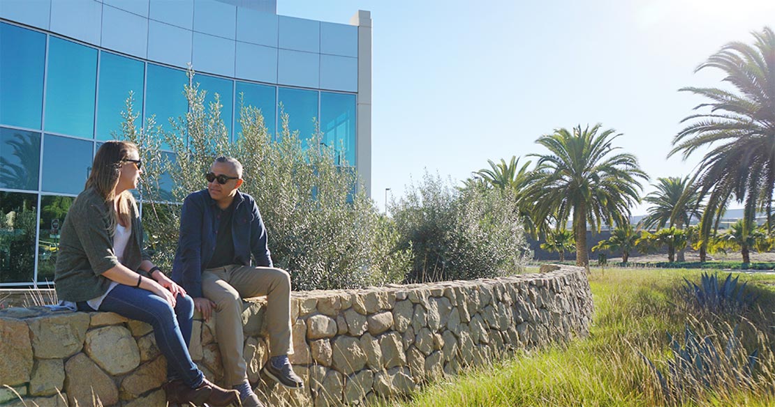 Two employees sitting on a stone wall outside of Deckers Brands global headquarters.