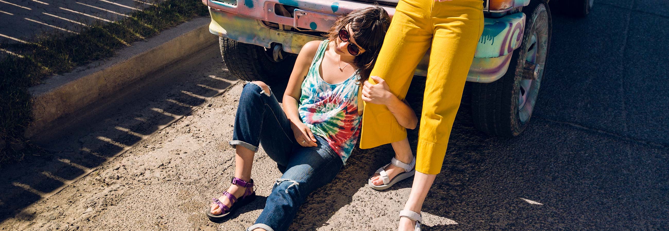Two women leaning against a car wearing Teva sandals.